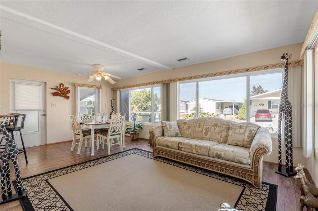 A living room with a dining area, beige sofa, wood-look flooring, and large windows — 533 FLEETWOOD STREET, NORTH PORT, FL