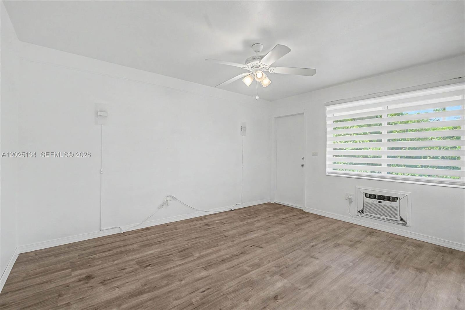 An empty room features white walls, wood-look flooring, a ceiling fan, and a window unit — 60 NW 79th St # 14, Miami FL 33150, MIAMI, FL
