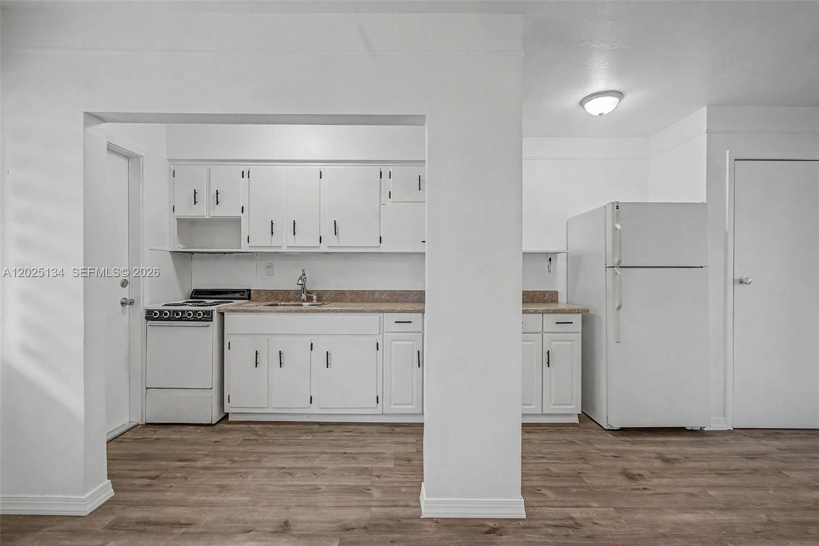 A kitchen features white cabinets, a stove, a refrigerator, and wood-look flooring — 60 NW 79th St # 14, Miami FL 33150, MIAMI, FL
