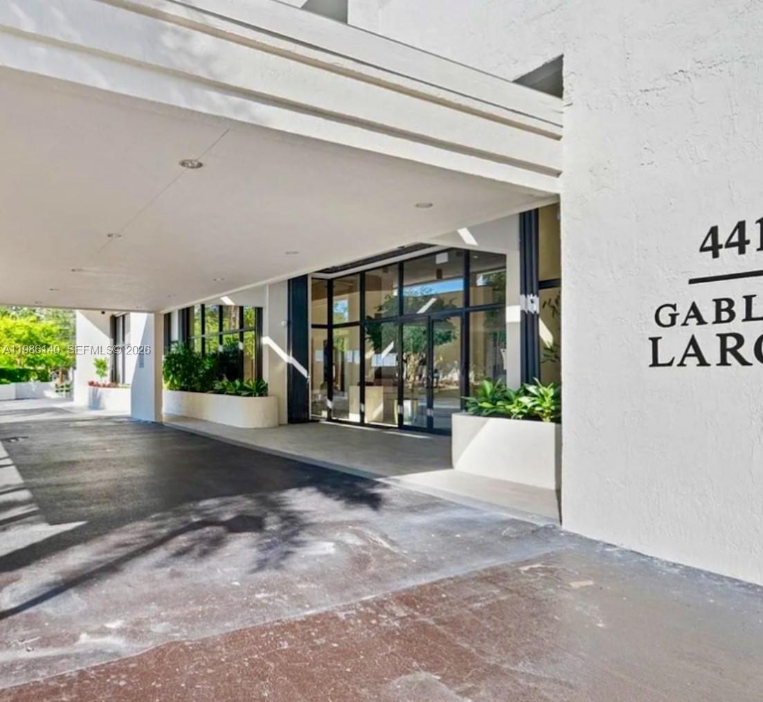 A covered driveway leads to the glass-fronted entrance of a modern building with white walls — 441 Valencia Ave # 803, Coral Gables FL 33134, CORAL GABLES, FL