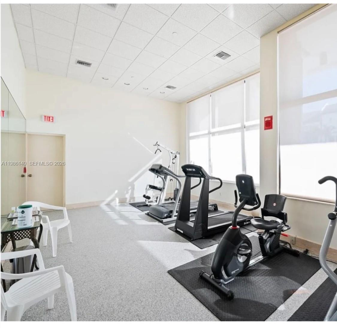 A bright fitness room features exercise equipment, white walls, large windows, and white plastic chairs — 441 Valencia Ave # 803, Coral Gables FL 33134, CORAL GABLES, FL