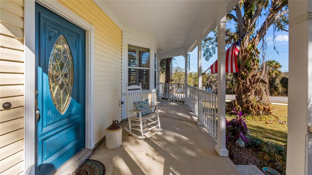 A covered front porch features a blue door, a rocking chair, and a hanging American flag — 110 W MINNEHAHA AVENUE, CLERMONT, FL