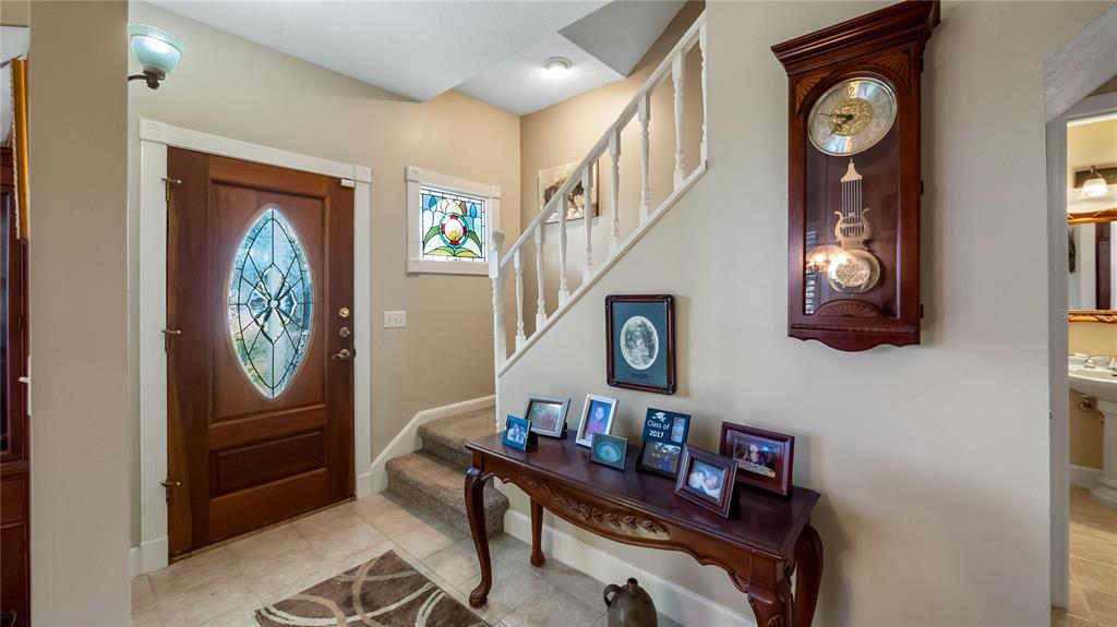 An entryway features a wooden front door, a staircase, a grandfather clock, and a console table — 110 W MINNEHAHA AVENUE, CLERMONT, FL