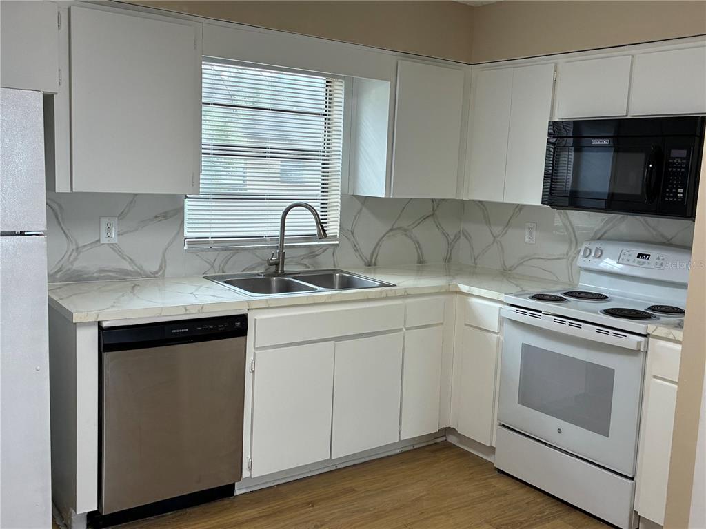 A kitchen features white cabinets, marble-patterned countertops, a stainless steel dishwasher, and white appliances — 5101 S CLARICE COURT UNIT 1C, TAMPA, FL