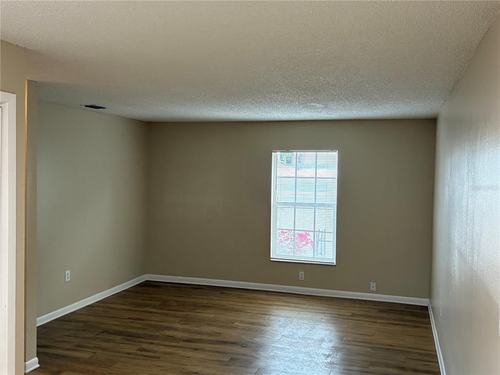 An empty room with beige walls, wood-look flooring, a single window, and a popcorn ceiling — 5101 S CLARICE COURT UNIT 1C, TAMPA, FL
