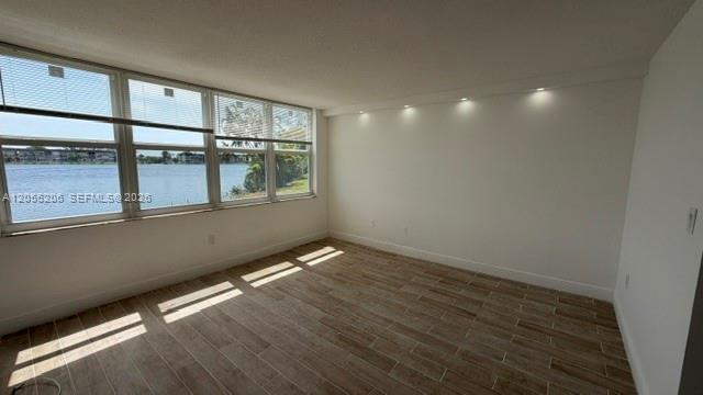An empty room with wood-look tile floors, recessed lighting, and large windows overlooking water — 1660 NE 191st St # 1, Miami FL 33179, MIAMI, FL