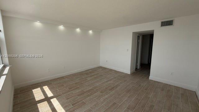 An empty room features light-colored wood-look tile flooring, white walls, and recessed ceiling lighting — 1660 NE 191st St # 1, Miami FL 33179, MIAMI, FL