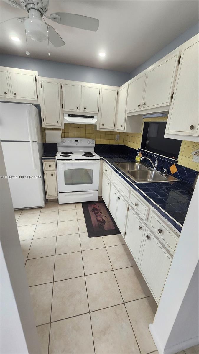 A kitchen features white cabinets, a white stove, a double sink, and blue tiled countertops — 4299 NW 16th St # 209, Lauderhill FL 33313, LAUDERHILL, FL