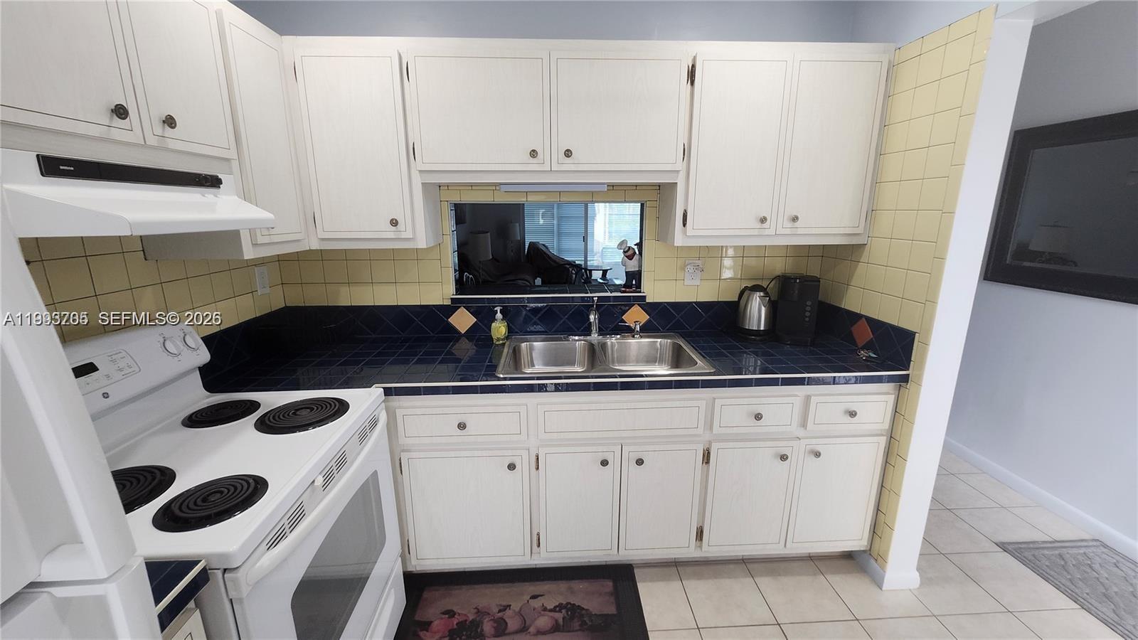 A kitchen features white cabinets, blue tiled countertops, and a pass-through window — 4299 NW 16th St # 209, Lauderhill FL 33313, LAUDERHILL, FL