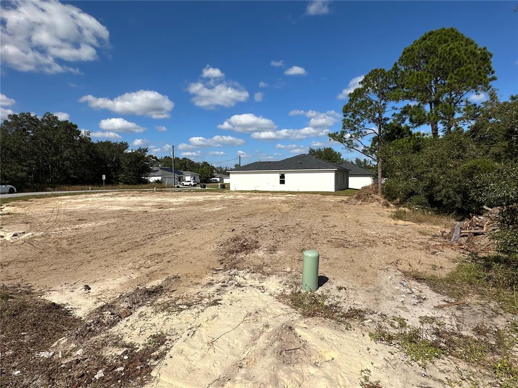 A vacant, cleared residential lot features a green utility pedestal and surrounding trees under blue skies — 105 TENCH DRIVE, KISSIMMEE, FL