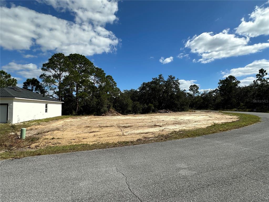 A cleared, sandy residential lot sits next to a white house under a blue sky — 105 TENCH DRIVE, KISSIMMEE, FL