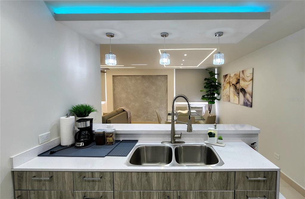 A modern kitchen features white countertops, wood-grain cabinets, and blue recessed ceiling lighting — Esperanza st. SANDY HILLS UNIT 16G, LUQUILLO, PR