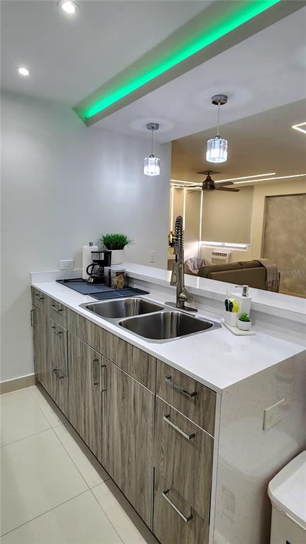 A kitchen sink and counter overlook a living area with modern lighting and wood-grain cabinets — Esperanza st. SANDY HILLS UNIT 16G, LUQUILLO, PR