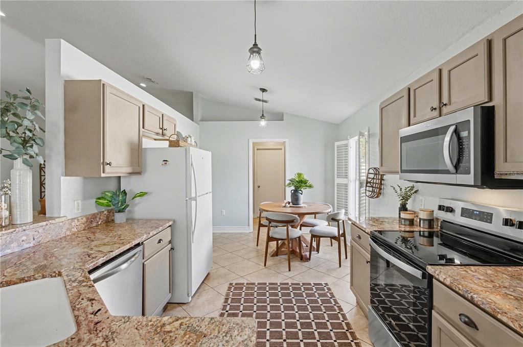 A kitchen features light-toned cabinets, granite countertops, stainless steel appliances, and a dining area — 2709 SE 45TH AVENUE, OCALA, FL