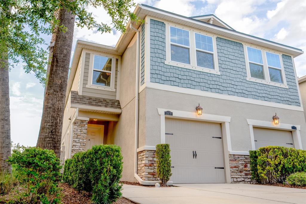 A two-story townhouse exterior features a beige stucco facade, blue shingle siding, and a garage — 11670 CAMBIUM CROWN DRIVE, RIVERVIEW, FL