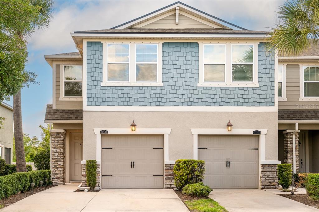 A two-story townhouse exterior features blue shingle siding, beige stucco, and two attached garages — 11670 CAMBIUM CROWN DRIVE, RIVERVIEW, FL