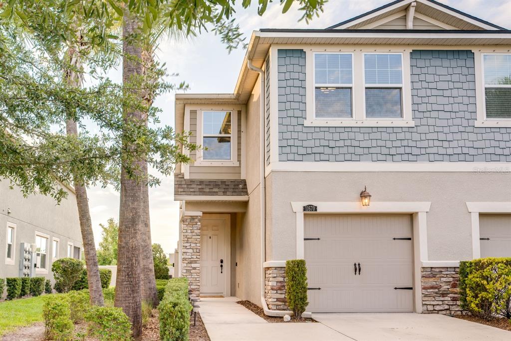 A two-story townhouse exterior features a beige garage, stone accents, and blue shingle siding — 11670 CAMBIUM CROWN DRIVE, RIVERVIEW, FL