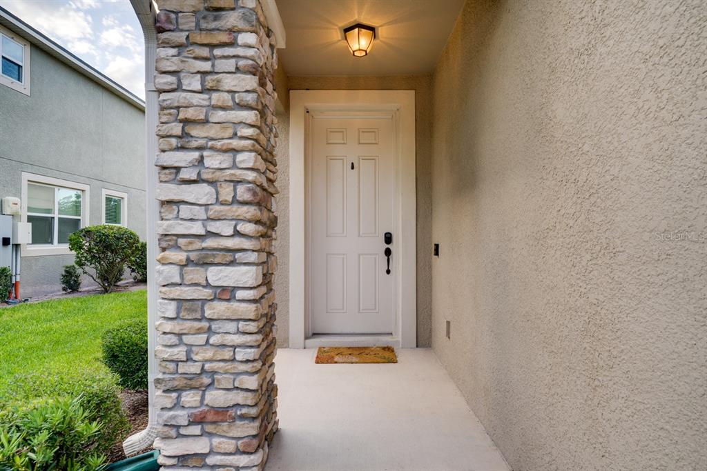 A white front door is set within a covered entryway featuring a stone pillar — 11670 CAMBIUM CROWN DRIVE, RIVERVIEW, FL