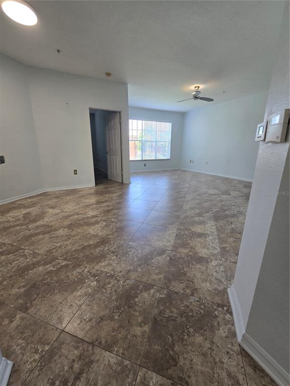 An open-concept living area features light-colored walls, a ceiling fan, and large brown floor tiles — 5506 METROWEST BOULEVARD UNIT 13-103, ORLANDO, FL