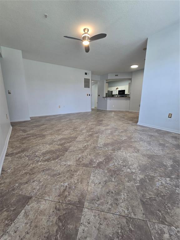 An open-concept living area features large square floor tiles and a ceiling fan — 5506 METROWEST BOULEVARD UNIT 13-103, ORLANDO, FL