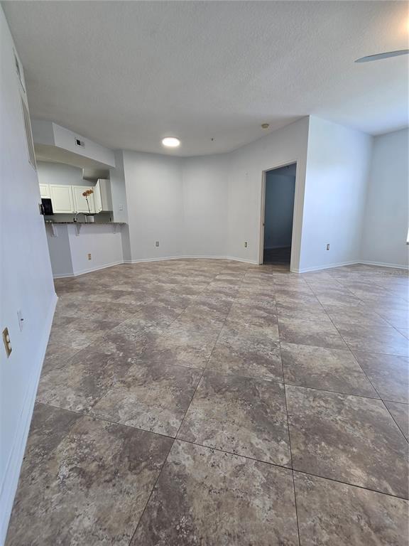 An open-concept living area features light gray walls, a kitchen breakfast bar, and tiled flooring — 5506 METROWEST BOULEVARD UNIT 13-103, ORLANDO, FL