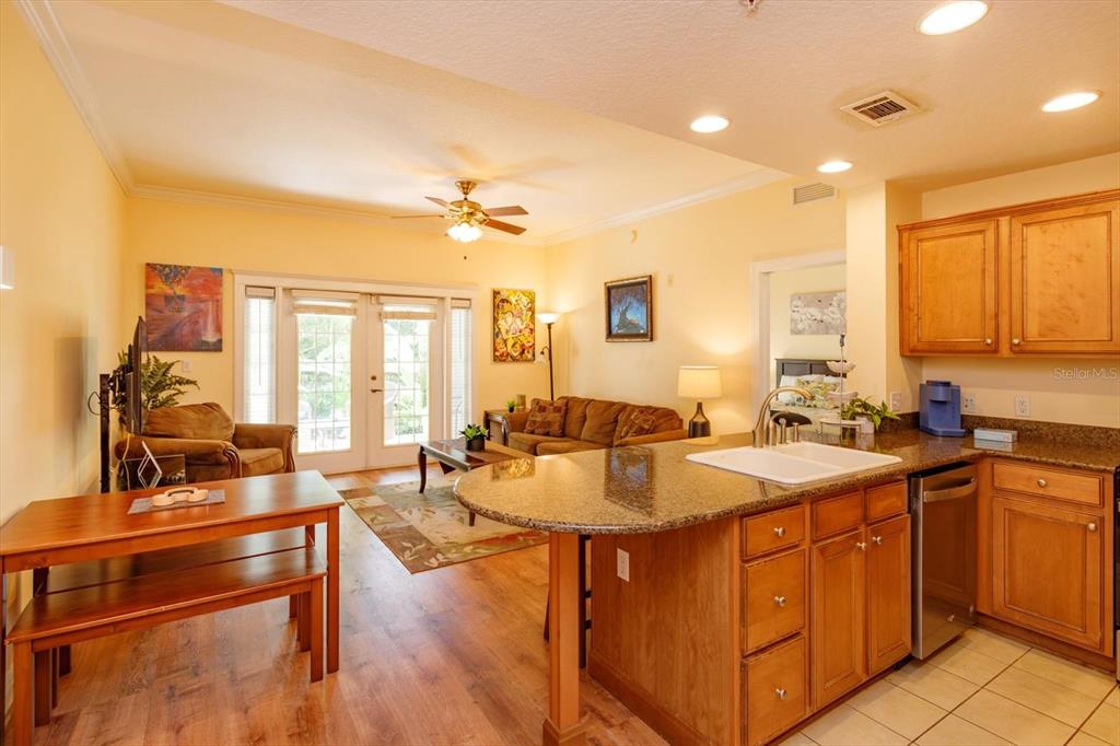 An open-concept kitchen with granite countertops overlooks a living room with wood-look flooring — 7644 HERITAGE CROSSING WAY UNIT 102, REUNION, FL