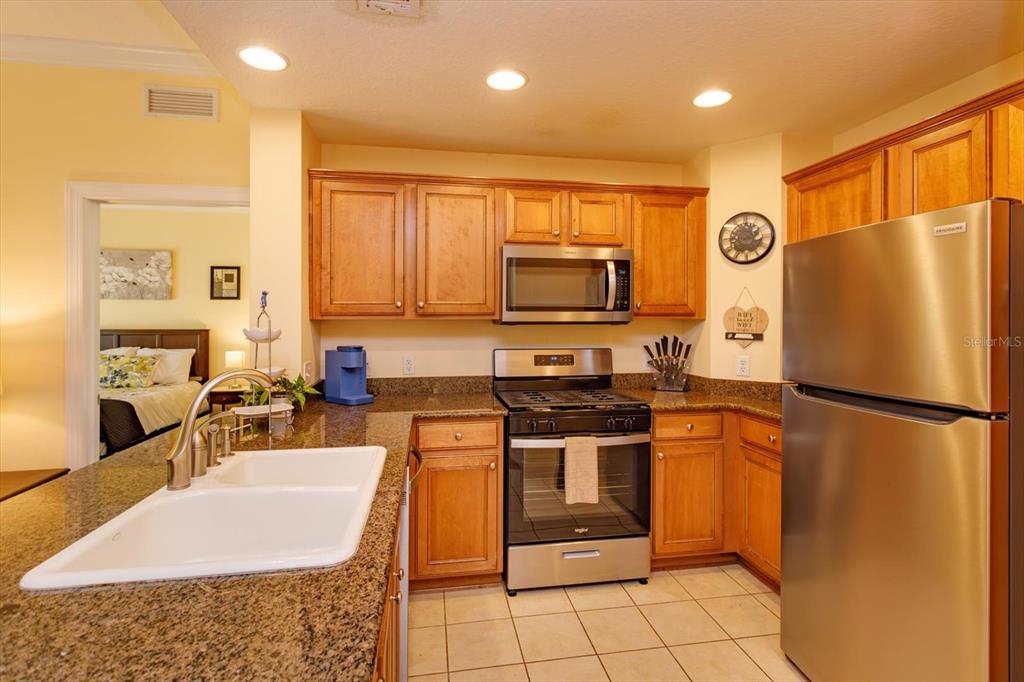 A kitchen with wood cabinets, granite countertops, and stainless steel appliances — 7644 HERITAGE CROSSING WAY UNIT 102, REUNION, FL