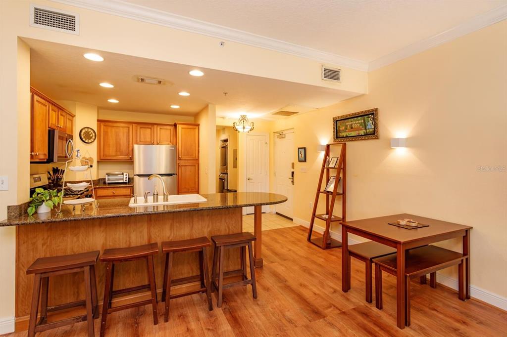A kitchen with wood cabinets and a breakfast bar overlooks a small dining area — 7644 HERITAGE CROSSING WAY UNIT 102, REUNION, FL