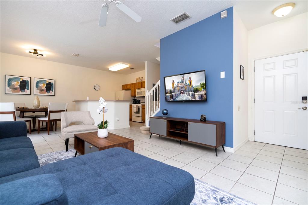 A living room features a blue accent wall with a mounted television and tiled floors — 3022 WHITE ORCHID ROAD, KISSIMMEE, FL