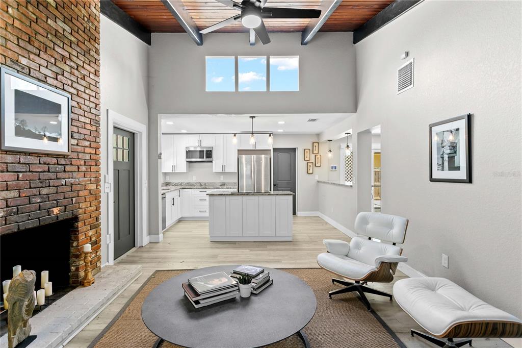 A living room with a brick fireplace, white kitchen, and vaulted ceiling with exposed beams — 520 LAKE MAGGIORE BOULEVARD S, ST PETERSBURG, FL