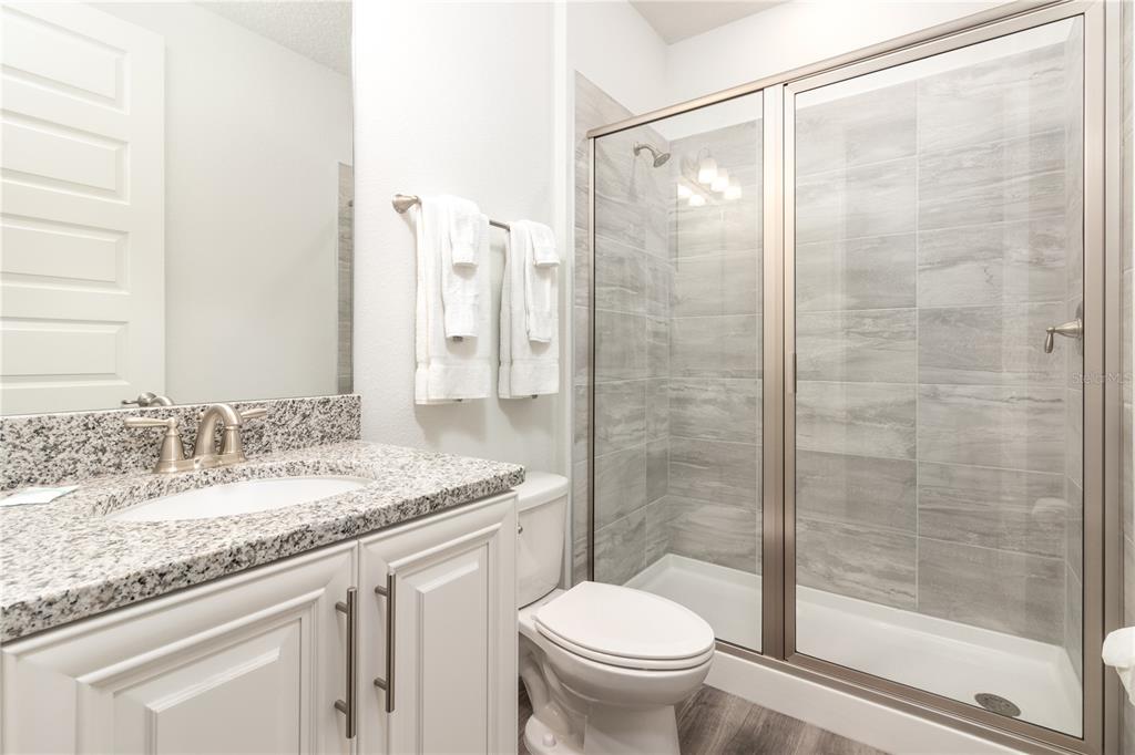 A bathroom features a granite vanity, white cabinets, a toilet, and a glass-enclosed walk-in shower — 1136 CASTLE PINES COURT, REUNION, FL