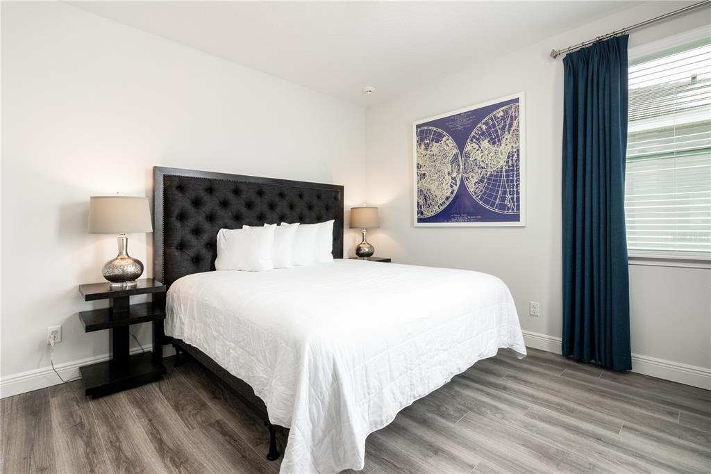 A bedroom features a tufted black headboard, white bedding, two nightstands, and blue curtains — 1136 CASTLE PINES COURT, REUNION, FL