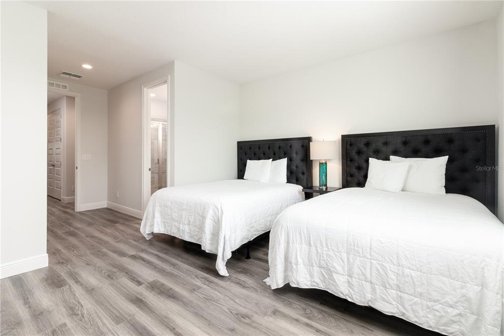 A bedroom features two beds with tufted black headboards, light wood-look flooring, and white walls — 1136 CASTLE PINES COURT, REUNION, FL