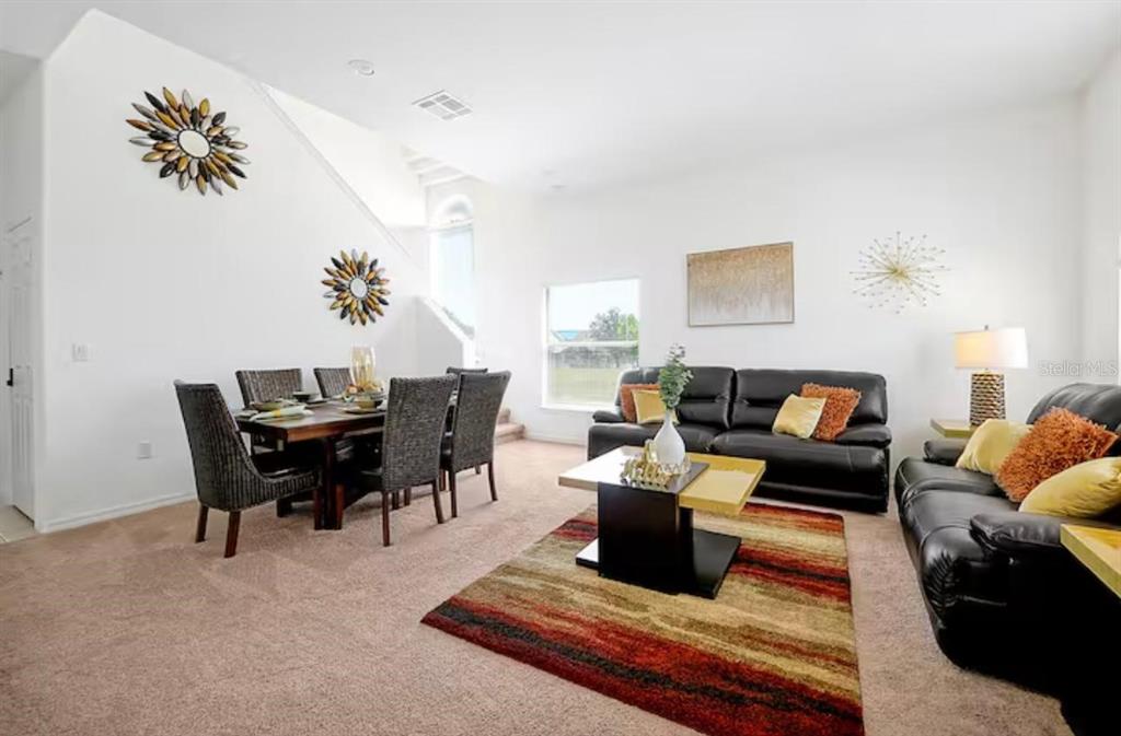 A living and dining room with black leather sofas, a wooden table, and carpeted floors — 559 CADIZ LOOP, DAVENPORT, FL