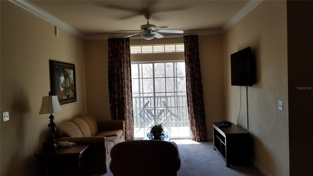 A living room features a tan sofa, a ceiling fan, and a sliding glass door — 8010 TUSCANY WAY UNIT 5308, DAVENPORT, FL