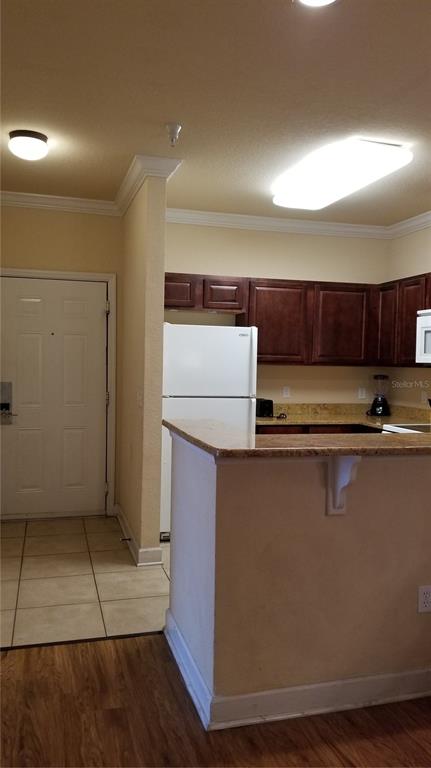 A kitchen with dark wood cabinets, a white refrigerator, and a granite-topped breakfast bar — 8010 TUSCANY WAY UNIT 5308, DAVENPORT, FL