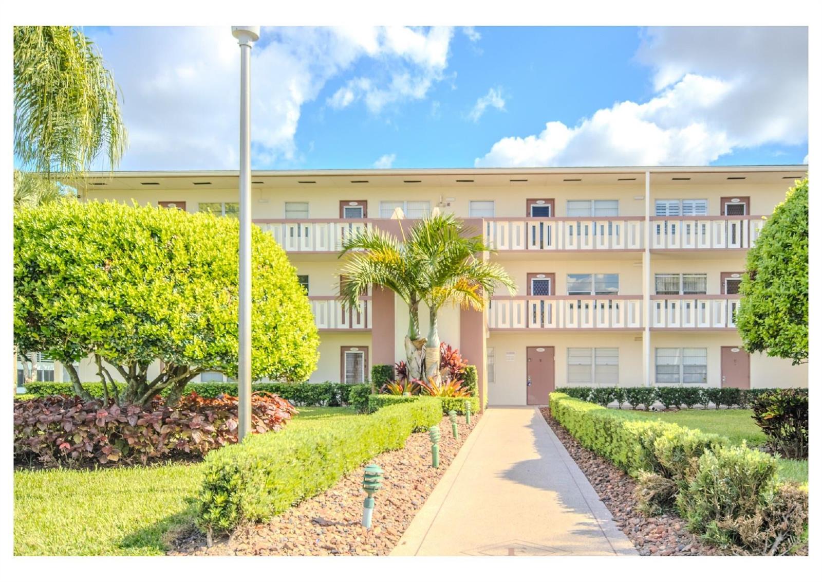 A three-story apartment building with a central walkway, palm trees, and manicured landscaping — 251 Preston F # 251, Boca Raton FL 33434, BOCA RATON, FL