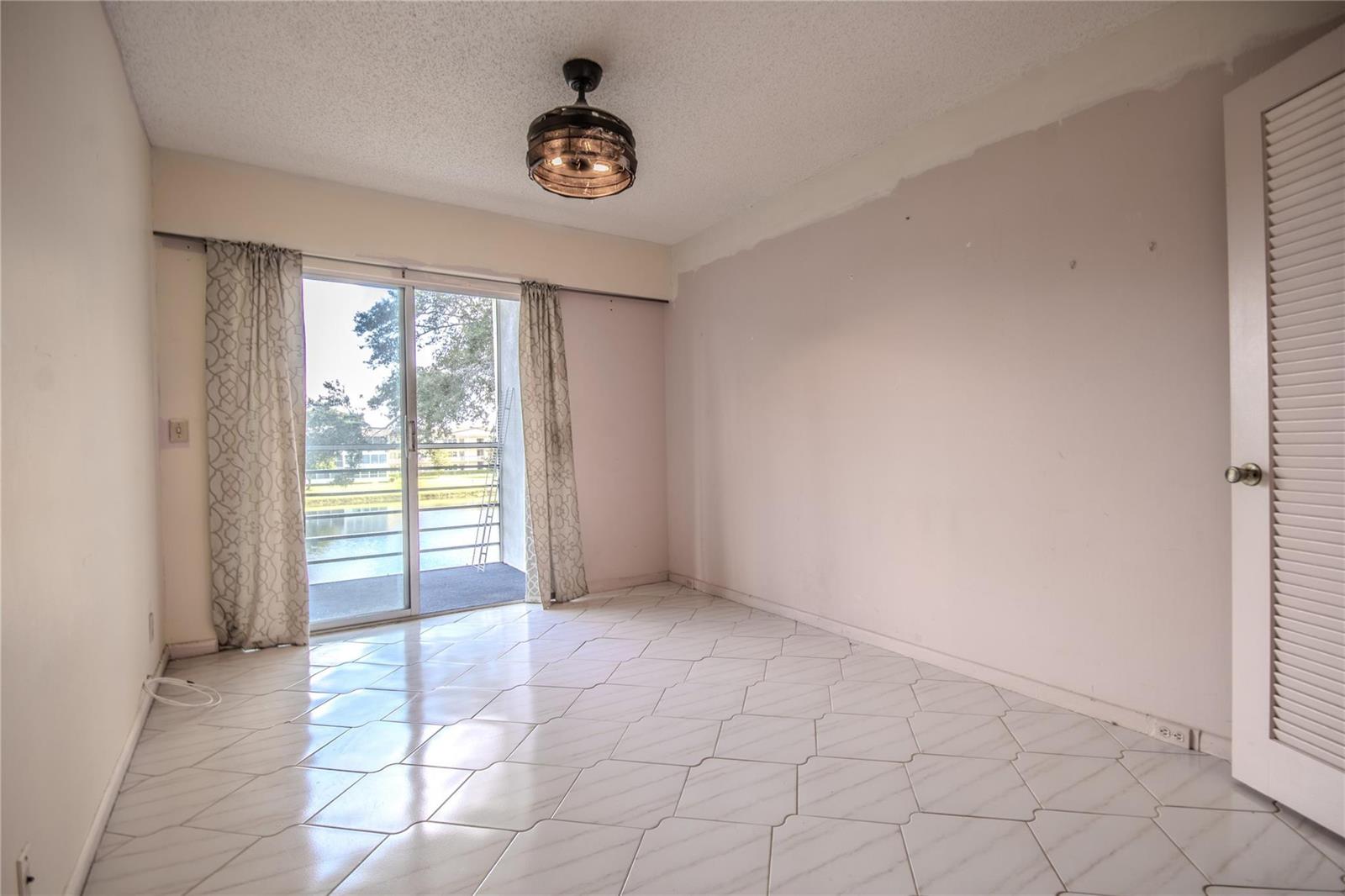 An empty bedroom with white tile floors, a ceiling light fixture, and a sliding glass door — 251 Preston F # 251, Boca Raton FL 33434, BOCA RATON, FL