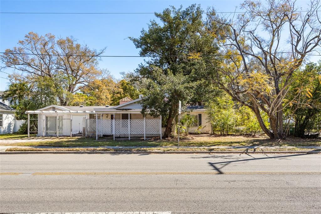A single-story house with a white lattice porch sits behind a road and large trees — 2627 W WATROUS AVENUE, TAMPA, FL