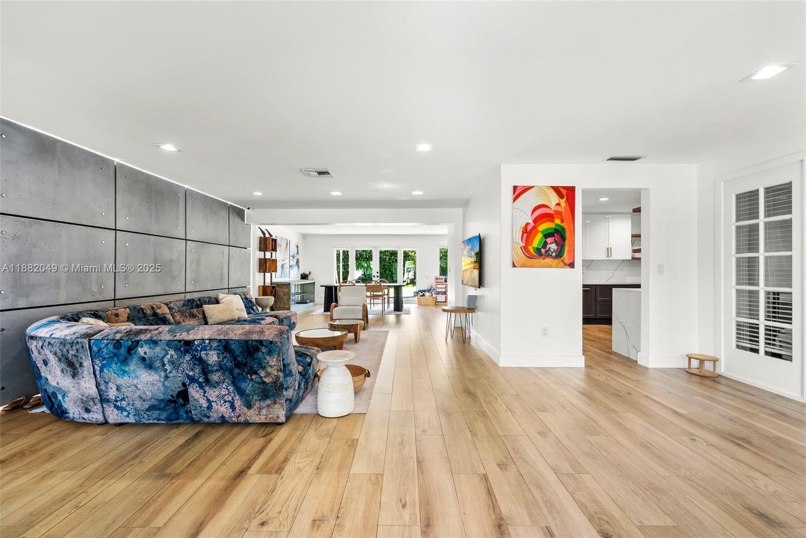 A living room features a patterned blue sofa, concrete wall panels, and light wood flooring — 21000 NE 18th Ct, Miami FL 33179, MIAMI, FL