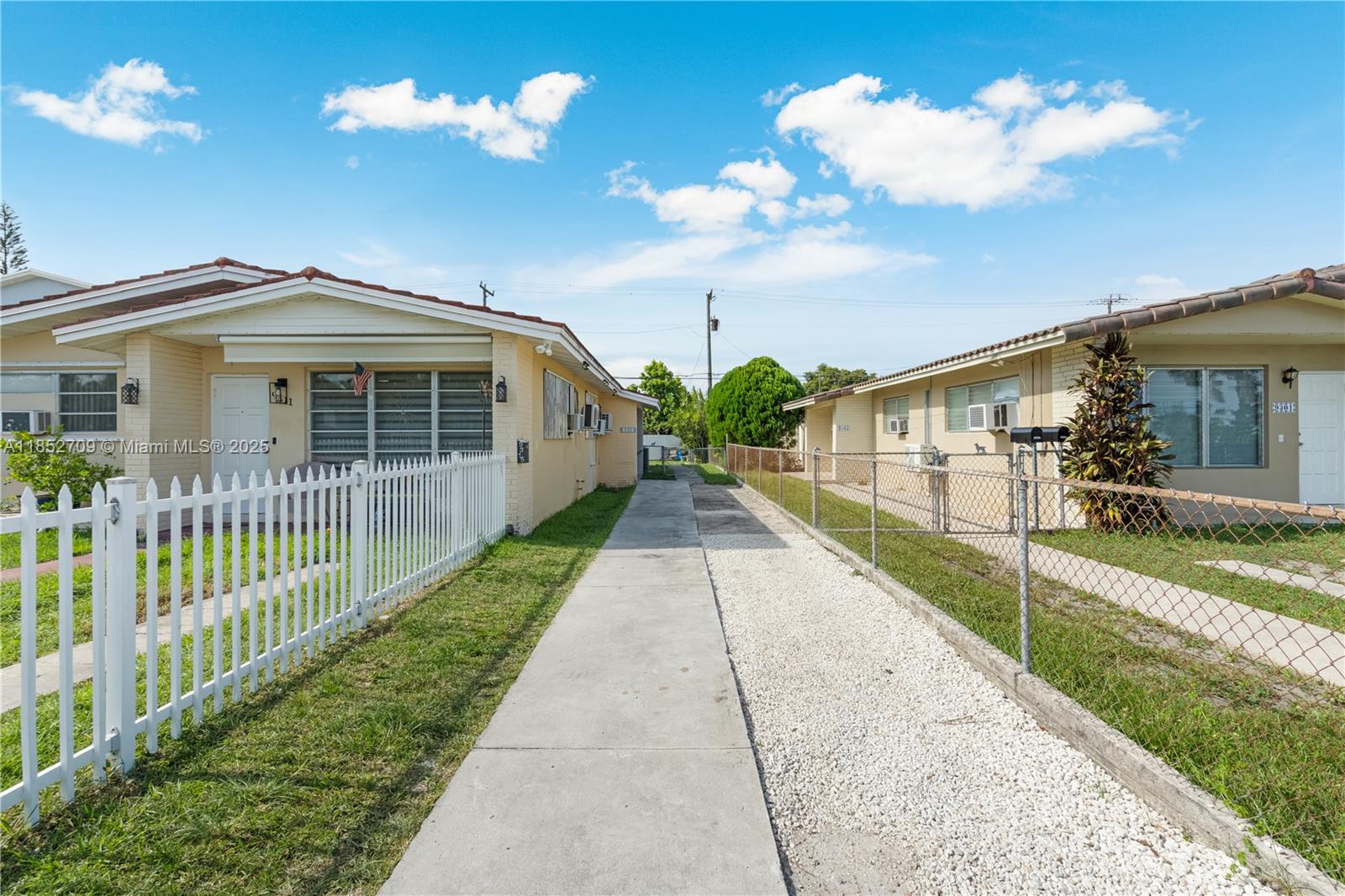 A concrete walkway separates two single-story houses with white fences and gravel driveways — 9311 SW 37th St, Miami FL 33165, MIAMI, FL