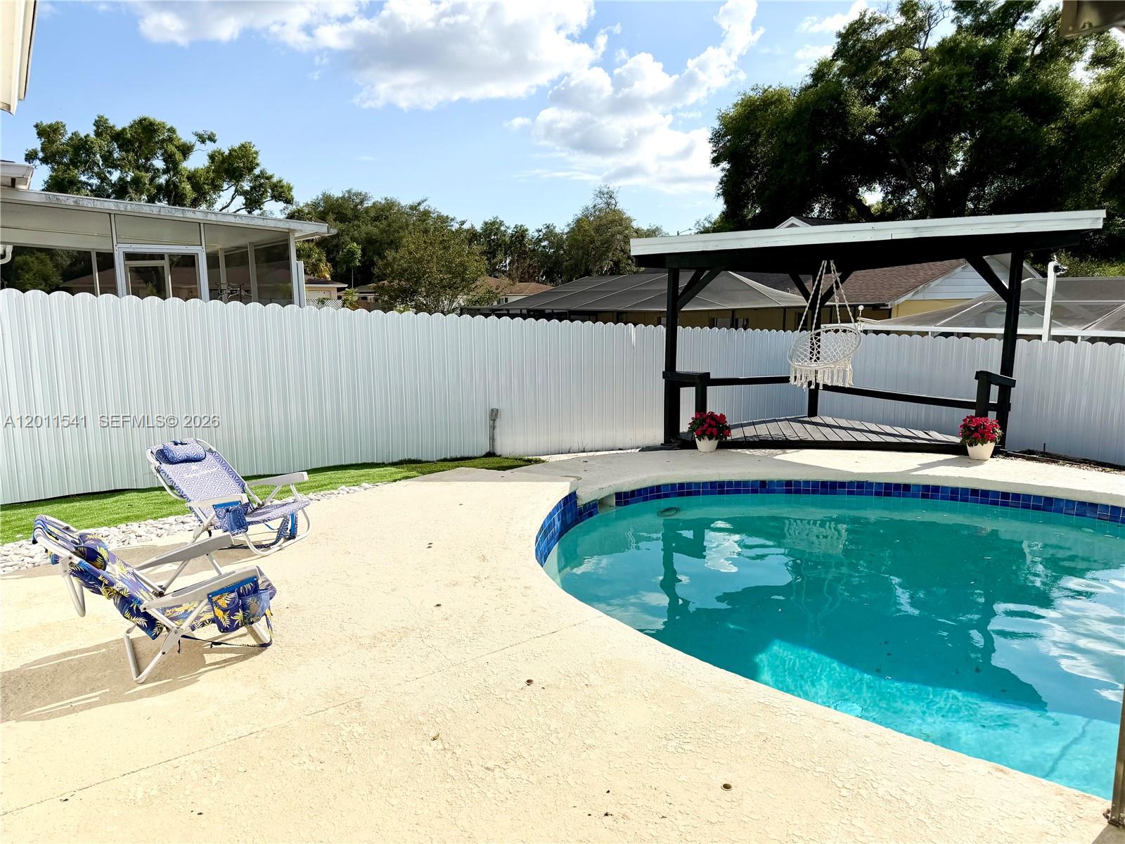 A backyard features a swimming pool, two lounge chairs, and a covered wooden deck structure — 143 VALLEY CIR, Tampa FL 33510, TAMPA, FL