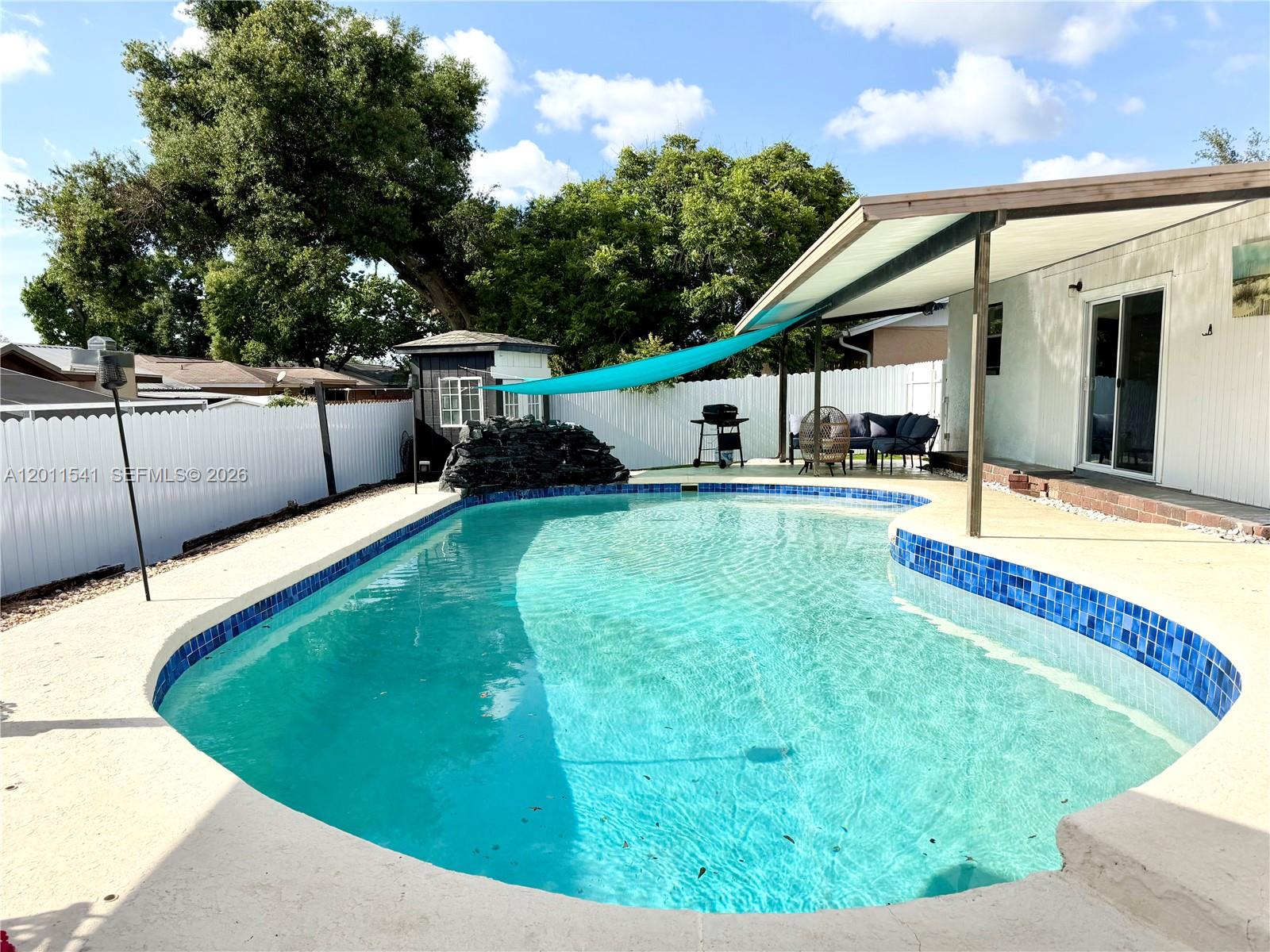 A backyard features a swimming pool with blue tile trim, a patio cover, and fencing — 143 VALLEY CIR, Tampa FL 33510, TAMPA, FL