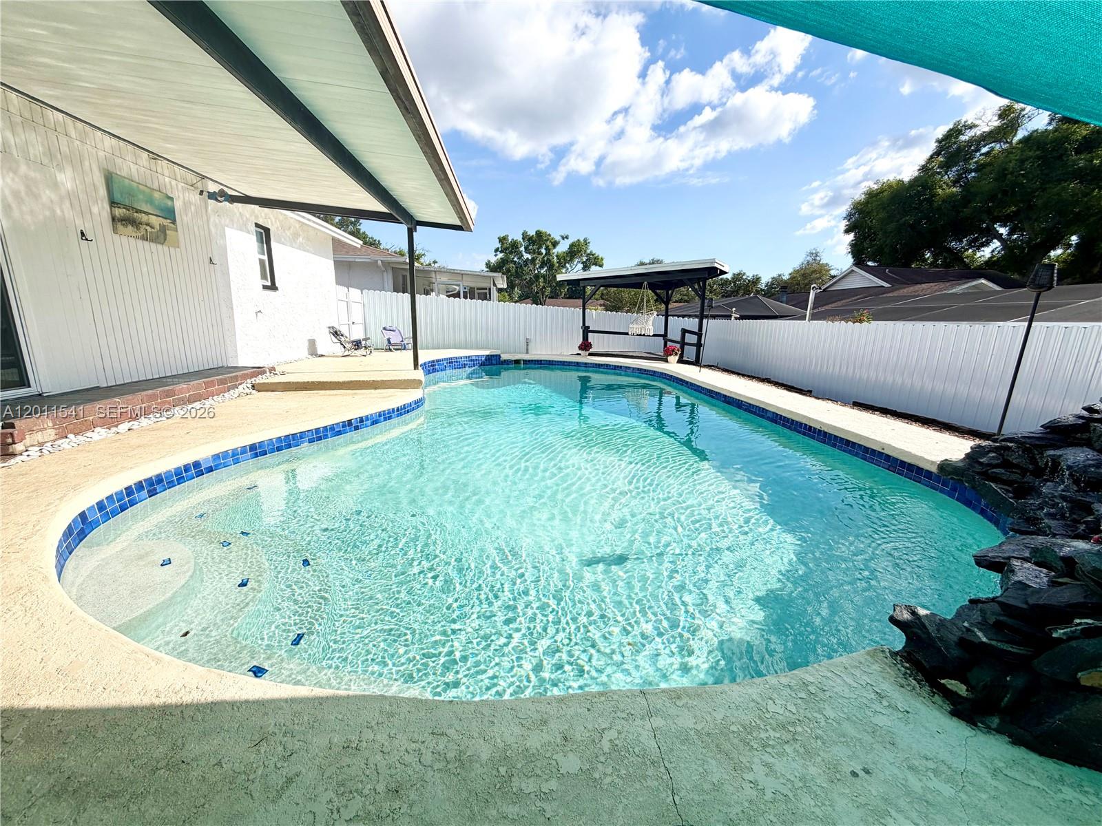 A backyard features a kidney-shaped swimming pool with a rock waterfall and a covered patio — 143 VALLEY CIR, Tampa FL 33510, TAMPA, FL