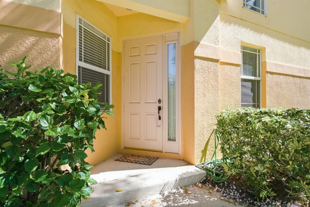 A beige exterior entrance with a white front door, side window, and surrounding landscaping — 1405 RIDGE TERRACE, TARPON SPRINGS, FL