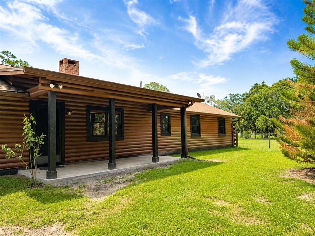A log cabin home features a covered porch, dark trim, and a brick chimney — 545 CHASE HAMMOCK ROAD, MERRITT ISLAND, FL