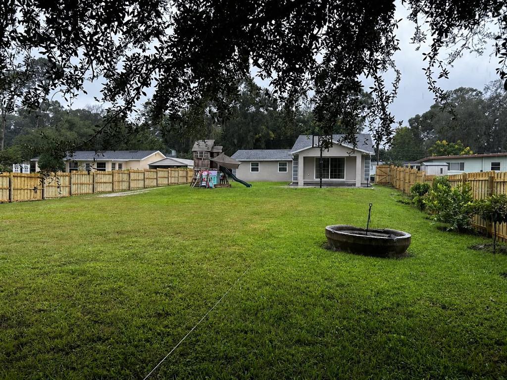 A large grassy backyard features a wooden playset, a concrete basin, and a wooden fence — 1150 MAGNOLIA DRIVE, ALTAMONTE SPRINGS, FL