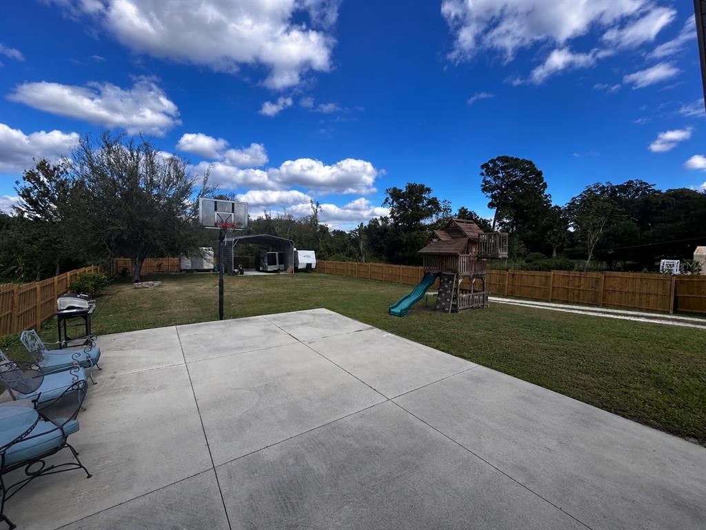 A concrete patio overlooks a large backyard featuring a basketball hoop and a wooden playset — 1150 MAGNOLIA DRIVE, ALTAMONTE SPRINGS, FL