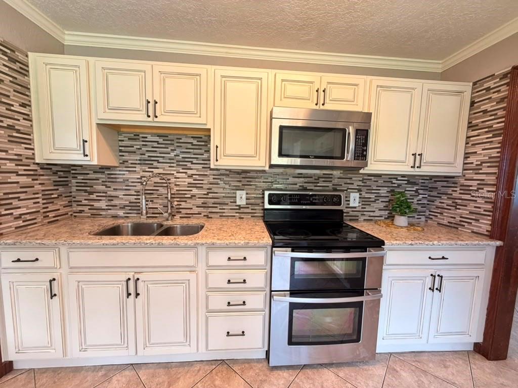 A kitchen features cream-colored cabinets, stainless steel appliances, a patterned tile backsplash, and granite countertops — 1150 MAGNOLIA DRIVE, ALTAMONTE SPRINGS, FL