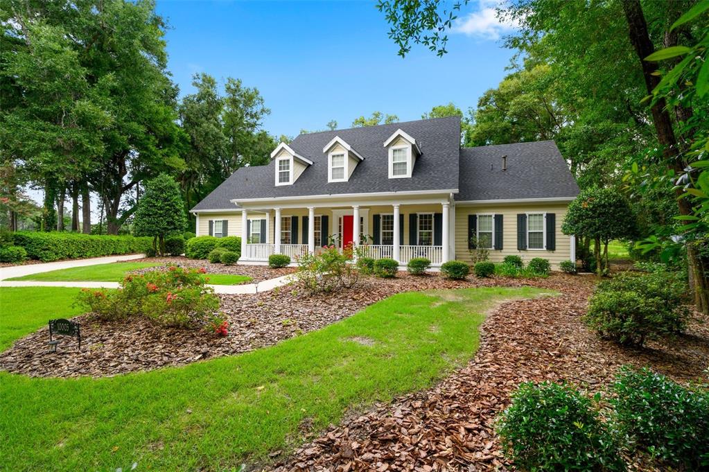 A yellow two-story house with a front porch, dormer windows, and a red front door — 10005 SW 48TH PLACE, GAINESVILLE, FL